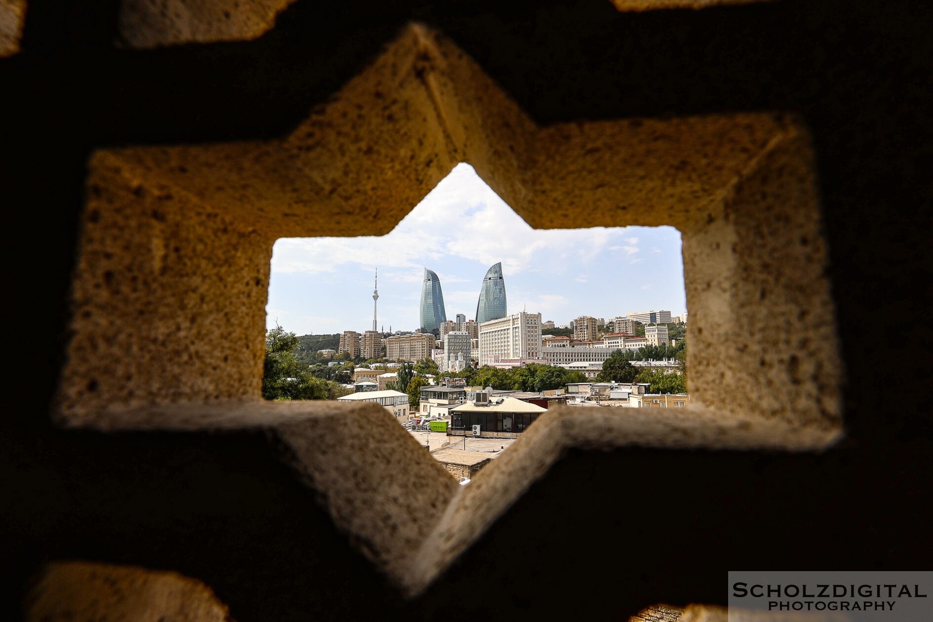Durch ein ornamentiertes Steinfenster fällt der Blick aus der Altstadt auf Baku und die Flame Towers.